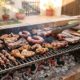 Diferentes tipos de carne a grelhar numa churrasqueira com brasas controladas